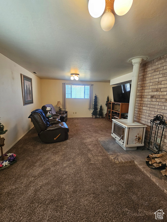 Carpeted living room with brick wall, ornate columns, a wood stove, and a textured ceiling