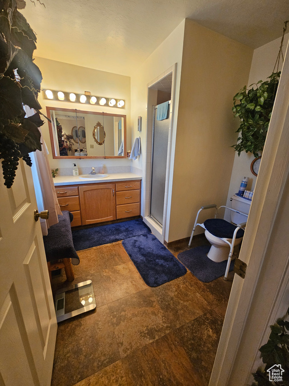 Bathroom featuring a shower with door, vanity, tile patterned flooring, and toilet