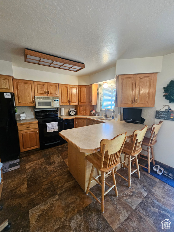 Kitchen featuring a textured ceiling, kitchen peninsula, black appliances, dark tile patterned flooring, and a kitchen breakfast bar