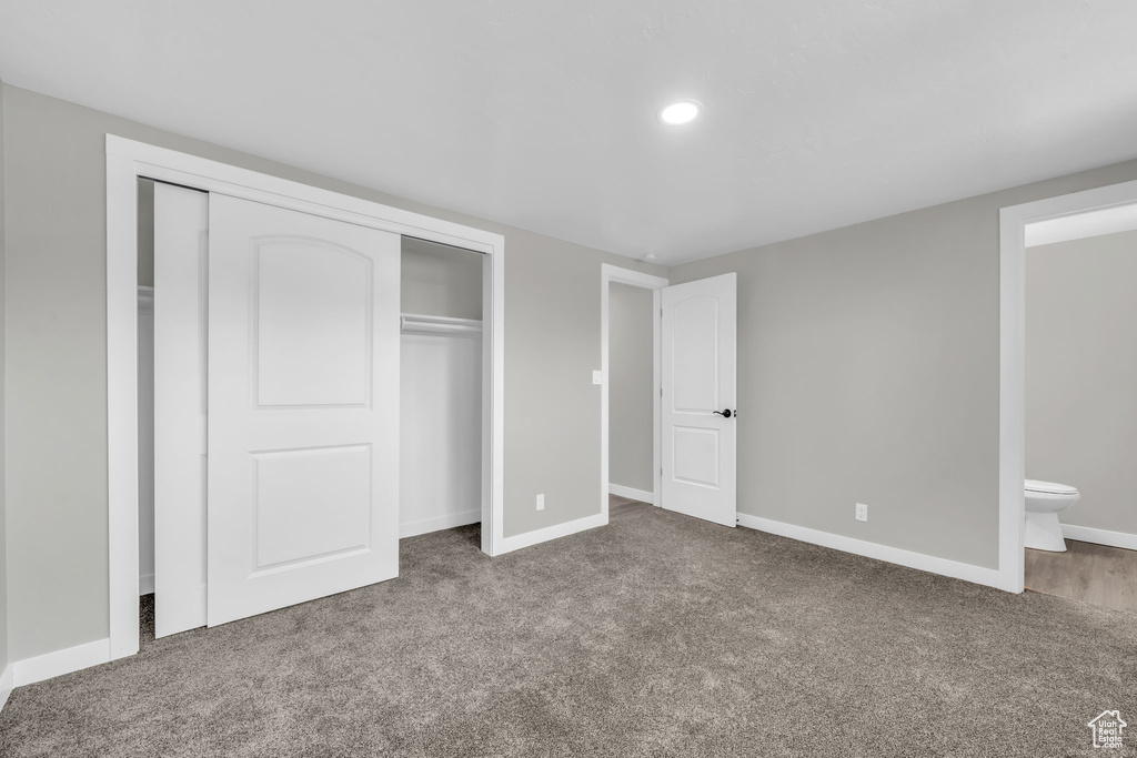 Unfurnished bedroom featuring dark colored carpet, a closet, and connected bathroom