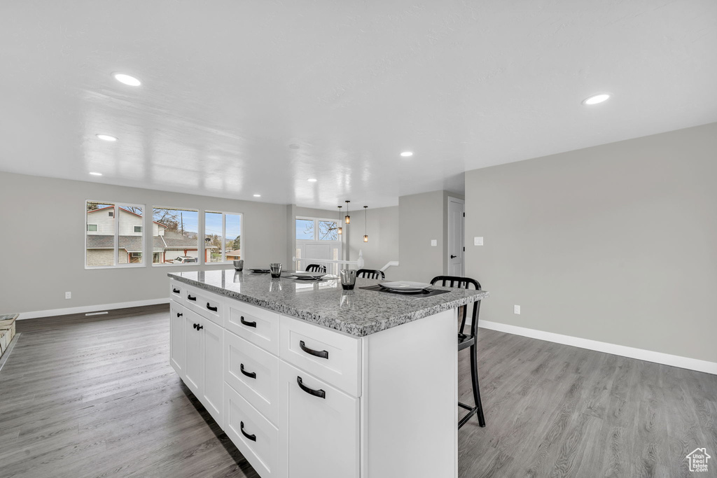 Kitchen featuring white cabinetry, hardwood / wood-style flooring, a kitchen bar, light stone counters, and a center island with sink