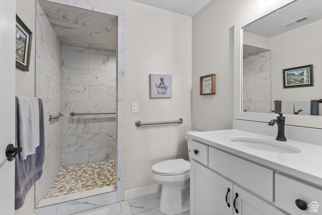 Bathroom with tiled shower, vanity, tile patterned flooring, and toilet