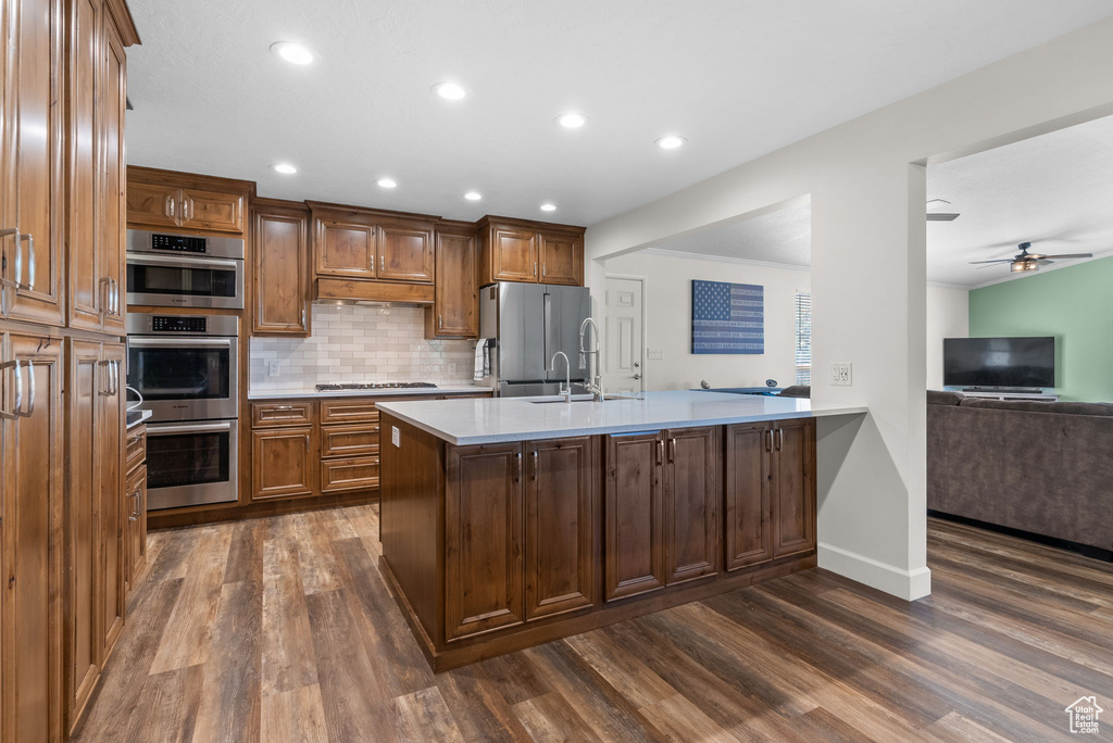 Kitchen featuring appliances with stainless steel finishes, kitchen peninsula, decorative backsplash, dark wood-type flooring, and ceiling fan