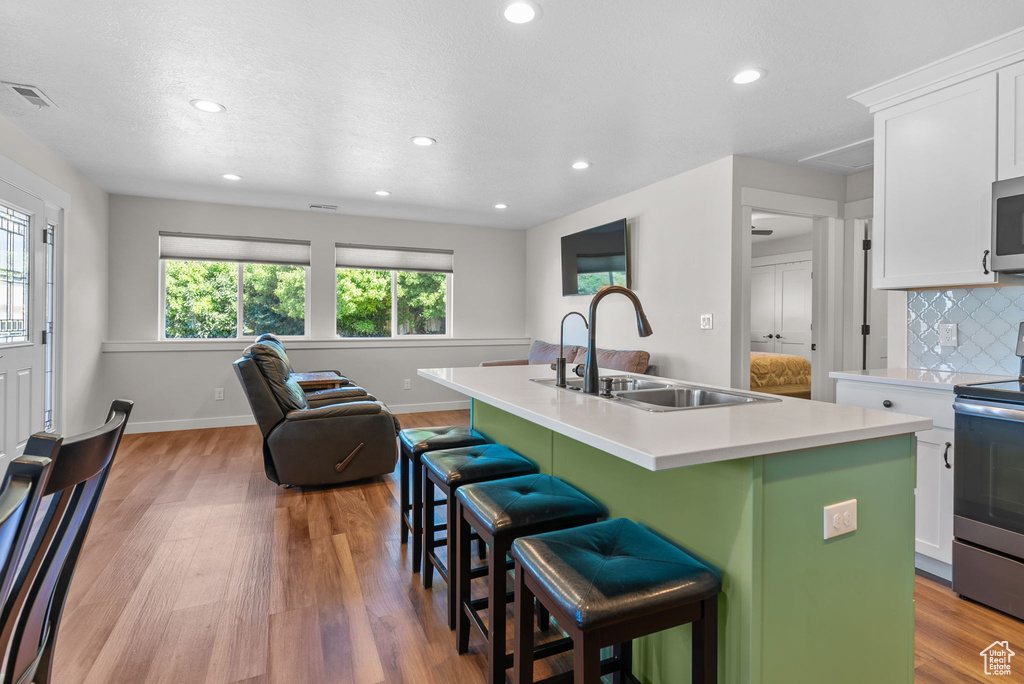 Kitchen with decorative backsplash, sink, a breakfast bar, light hardwood / wood-style flooring, and a kitchen island with sink