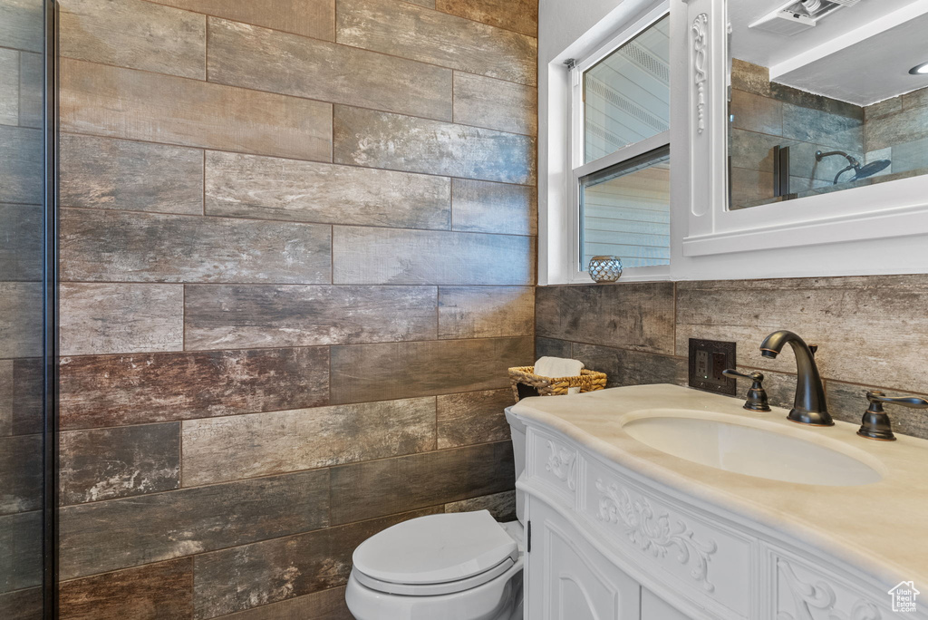 Bathroom featuring vanity, toilet, and tile walls