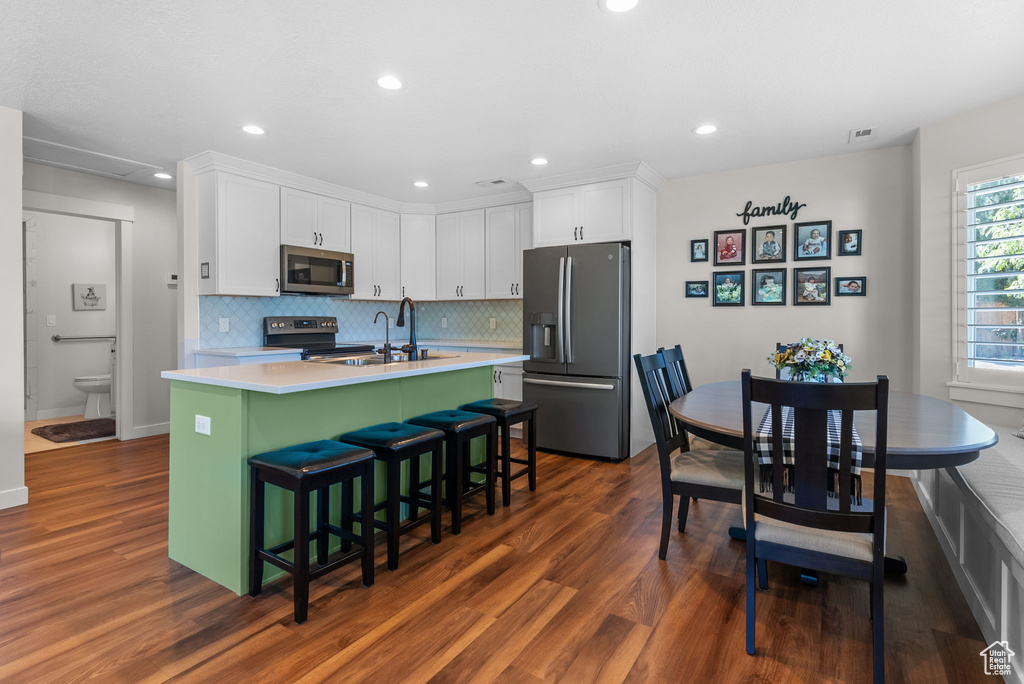 Kitchen featuring stainless steel appliances, decorative backsplash, white cabinets, an island with sink, and dark wood-type flooring