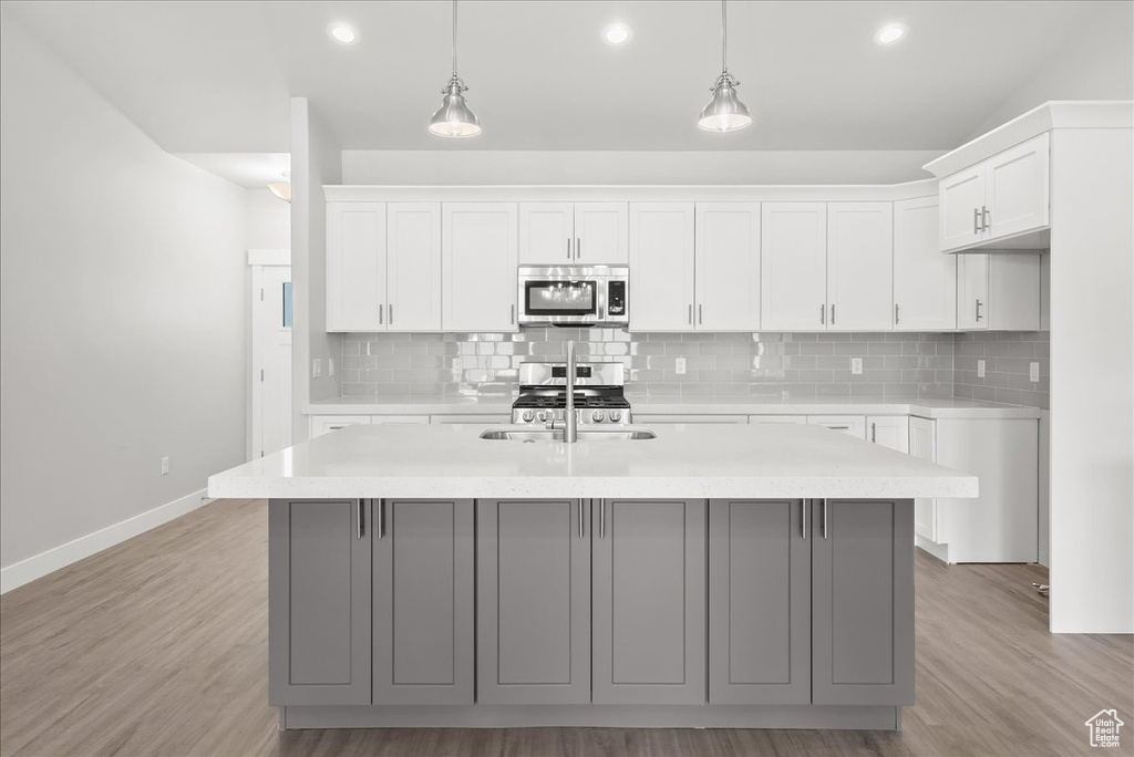 Kitchen with decorative light fixtures, white cabinetry, a center island with sink, and light wood-type flooring