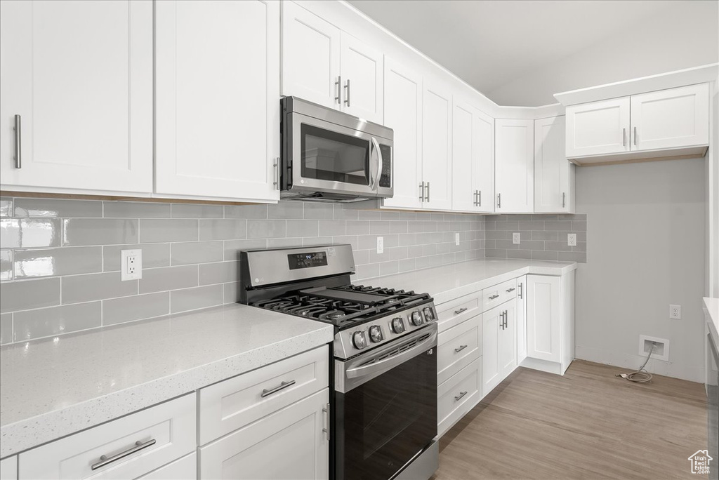 Kitchen featuring white cabinets, light stone counters, appliances with stainless steel finishes, light hardwood / wood-style flooring, and backsplash