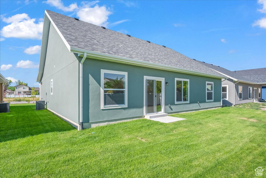 Rear view of house with central air condition unit and a lawn