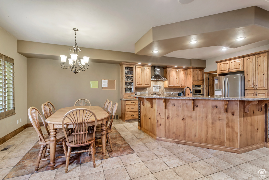 Kitchen with appliances with stainless steel finishes, backsplash, light tile patterned floors, and wall chimney range hood