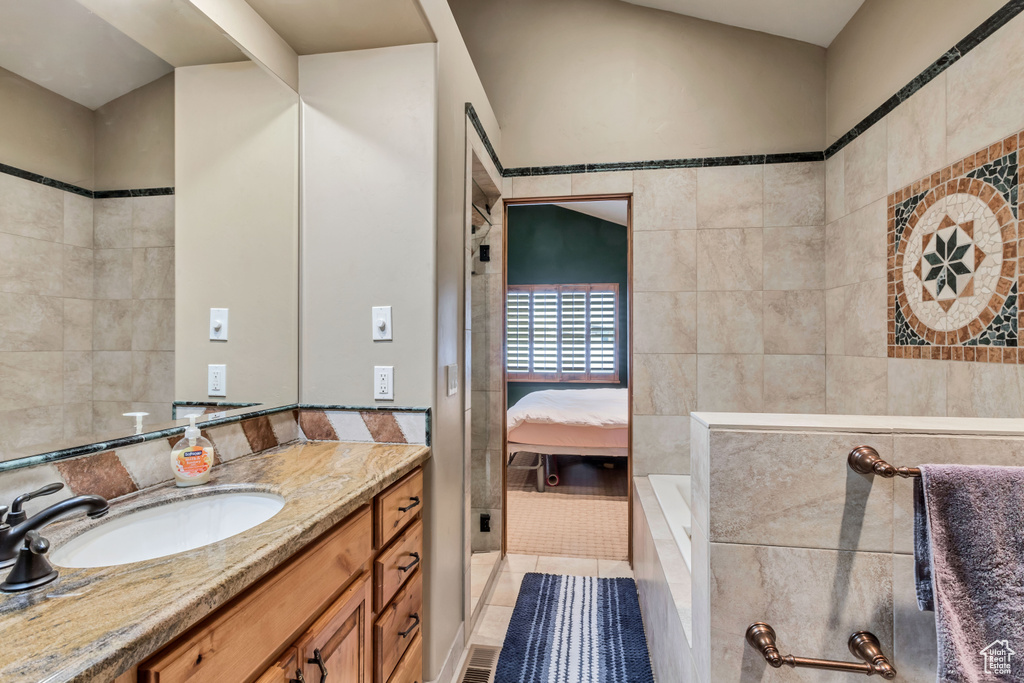 Bathroom with vanity, tile patterned flooring, tile walls, and a tub