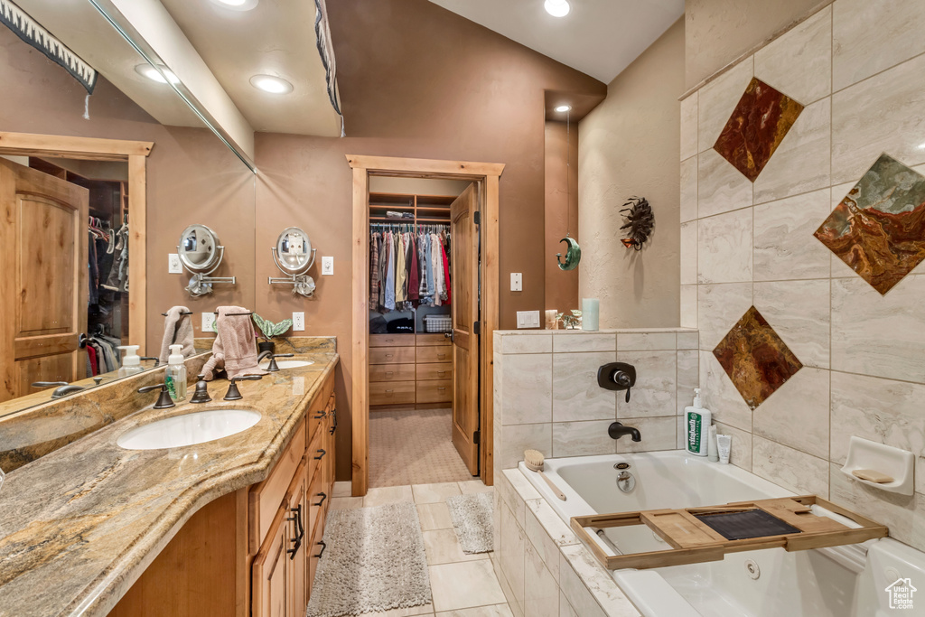 Bathroom featuring tiled tub, vanity, tile patterned flooring, and tile walls