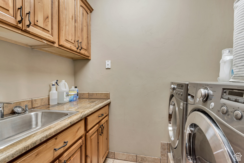 Clothes washing area featuring light tile patterned flooring, sink, cabinets, and independent washer and dryer