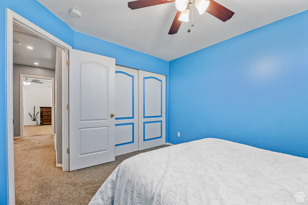 Carpeted bedroom featuring ceiling fan and a closet