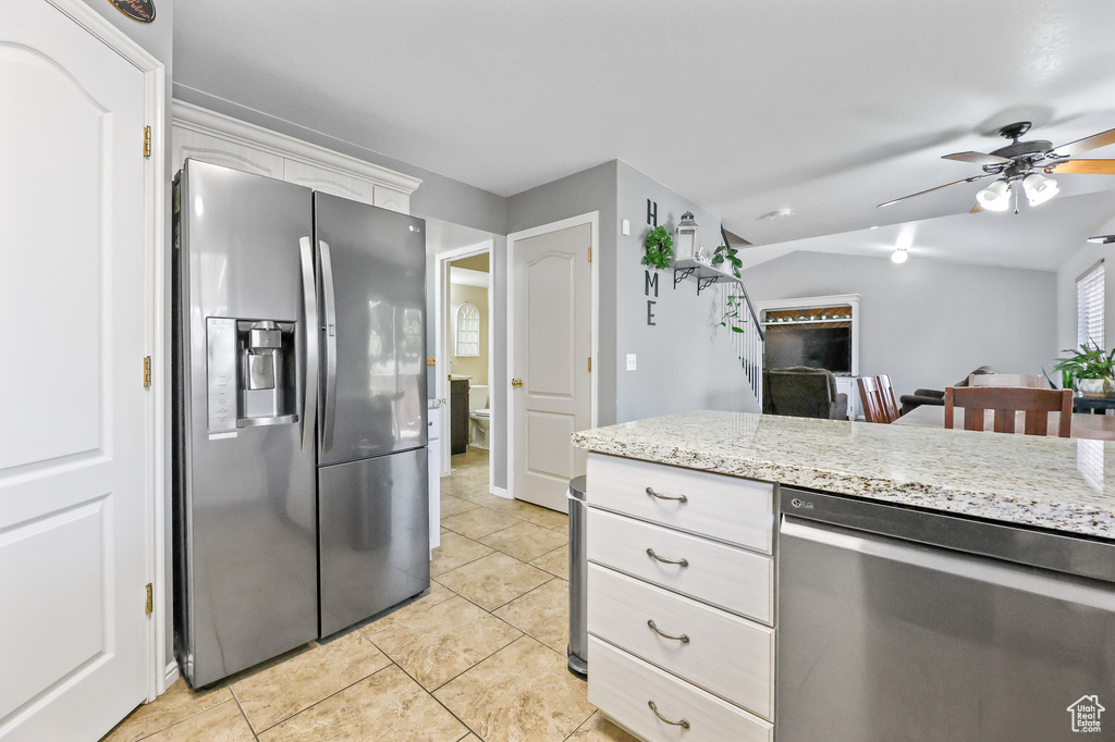 Kitchen featuring light tile patterned flooring, white cabinetry, ceiling fan, light stone countertops, and appliances with stainless steel finishes