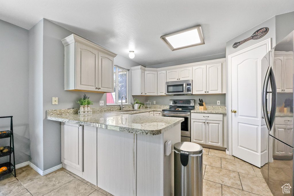 Kitchen featuring appliances with stainless steel finishes, sink, kitchen peninsula, light tile patterned floors, and light stone countertops