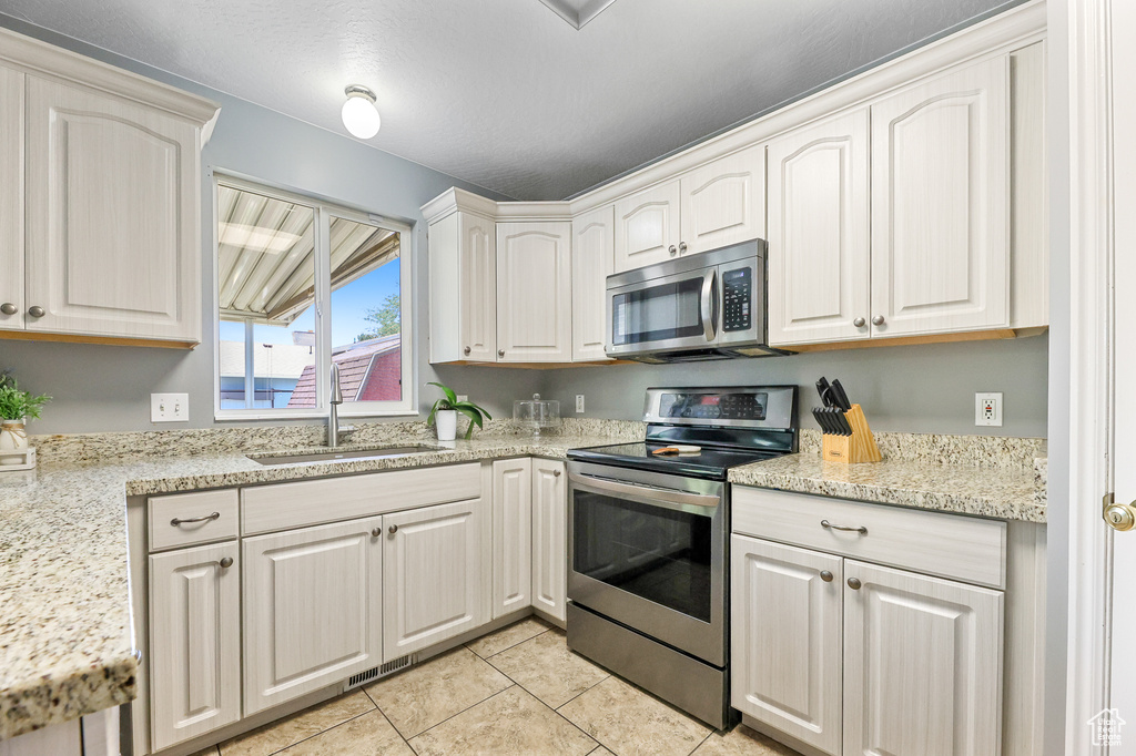 Kitchen with sink, light stone counters, stainless steel appliances, and light tile patterned floors