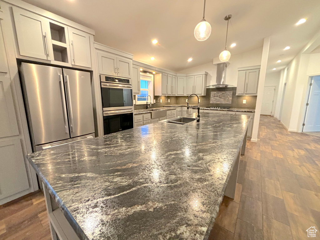 Kitchen featuring stainless steel appliances, backsplash, dark hardwood / wood-style floors, an island with sink, and wall chimney exhaust hood
