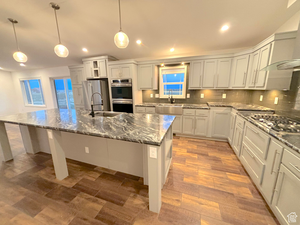 Kitchen with appliances with stainless steel finishes, wall chimney range hood, sink, decorative backsplash, and an island with sink