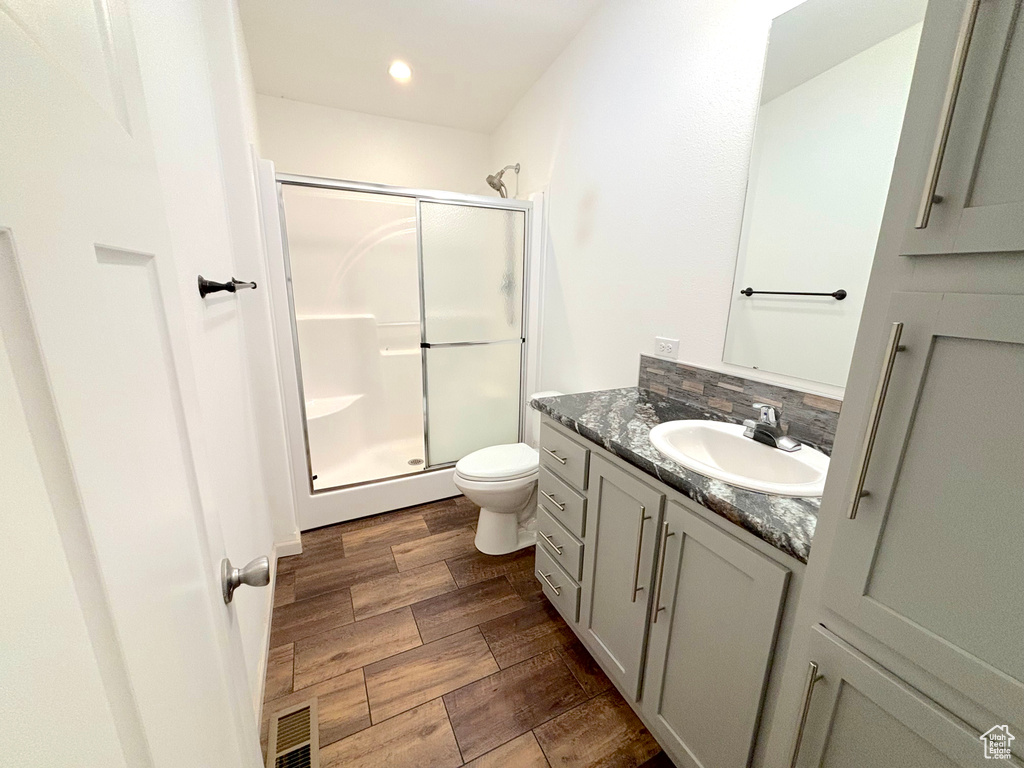 Bathroom featuring vanity, wood-type flooring, tasteful backsplash, a shower with shower door, and toilet