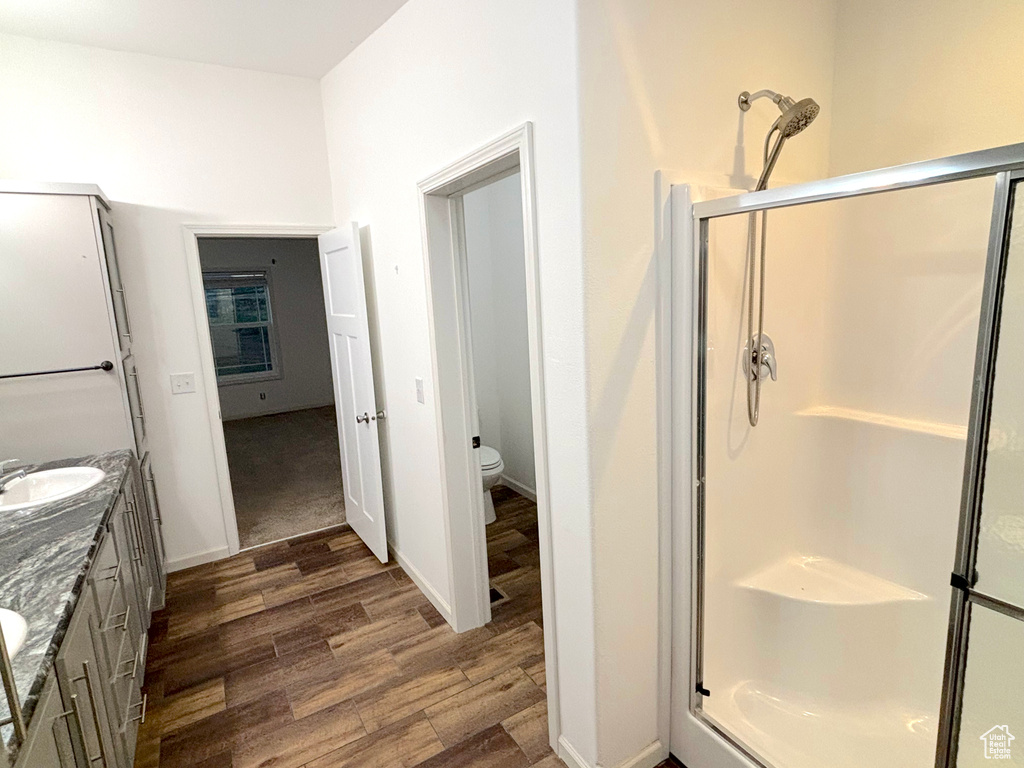 Bathroom featuring hardwood / wood-style floors, dual vanity, a shower with shower door, and toilet