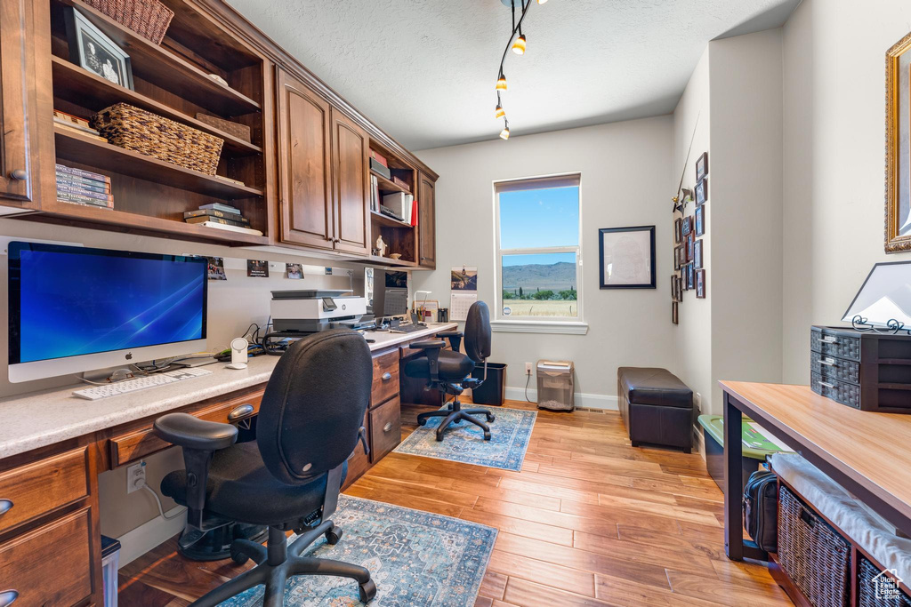 Office space with a textured ceiling, rail lighting, light wood-type flooring, and built in desk