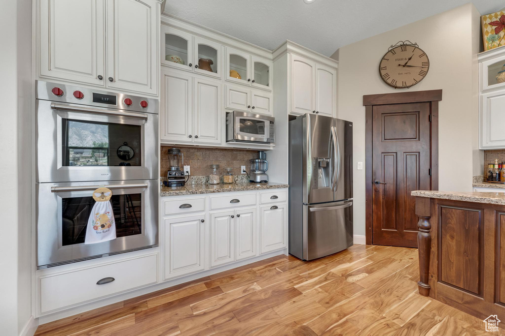 Kitchen featuring light hardwood / wood-style flooring, tasteful backsplash, white cabinets, light stone countertops, and appliances with stainless steel finishes