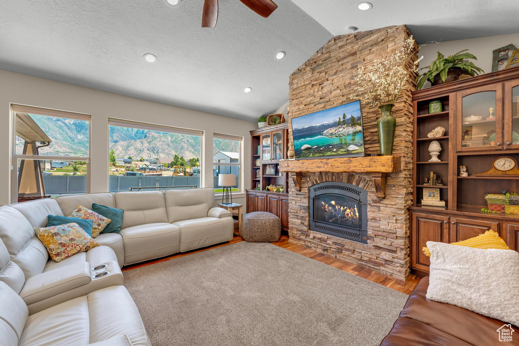 Living room featuring light hardwood / wood-style flooring, vaulted ceiling, a fireplace, a textured ceiling, and ceiling fan