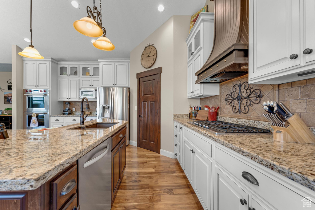 Kitchen featuring white cabinetry, light wood-type flooring, backsplash, appliances with stainless steel finishes, and sink