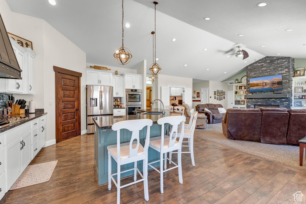 Kitchen with a breakfast bar, dark wood-type flooring, hanging light fixtures, appliances with stainless steel finishes, and a center island with sink