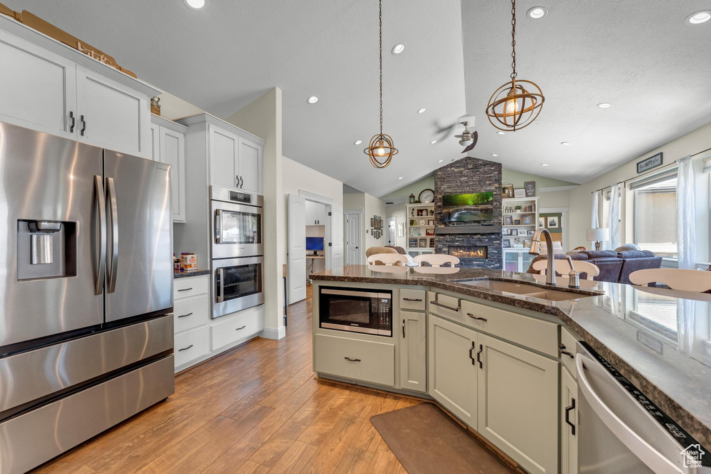 Kitchen featuring stainless steel appliances, hanging light fixtures, light wood-type flooring, sink, and vaulted ceiling