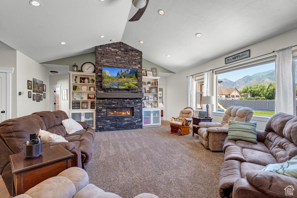 Carpeted living room with built in features, a mountain view, a stone fireplace, and high vaulted ceiling