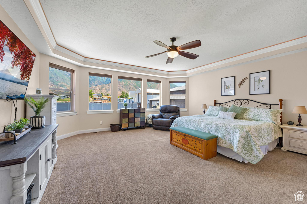 Carpeted bedroom featuring a textured ceiling, a raised ceiling, crown molding, and ceiling fan