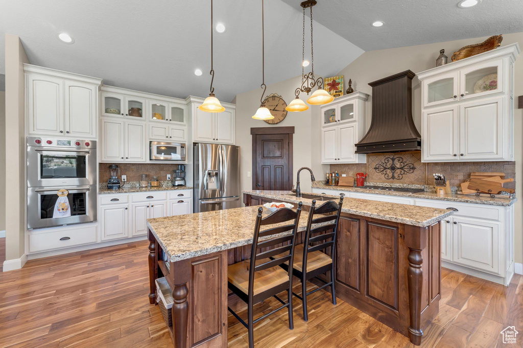 Kitchen featuring appliances with stainless steel finishes, custom exhaust hood, a center island with sink, and tasteful backsplash