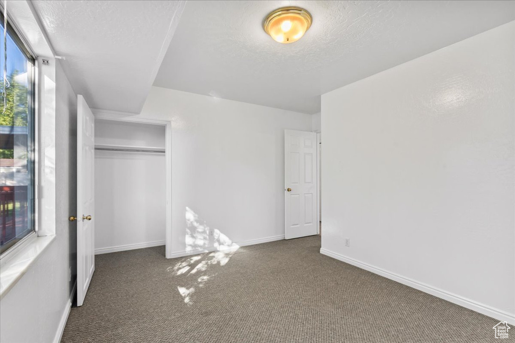 Unfurnished bedroom featuring a closet, a textured ceiling, and dark carpet