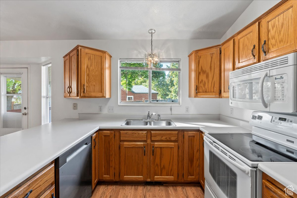 Kitchen featuring sink, light hardwood / wood-style floors, a notable chandelier, decorative light fixtures, and white appliances