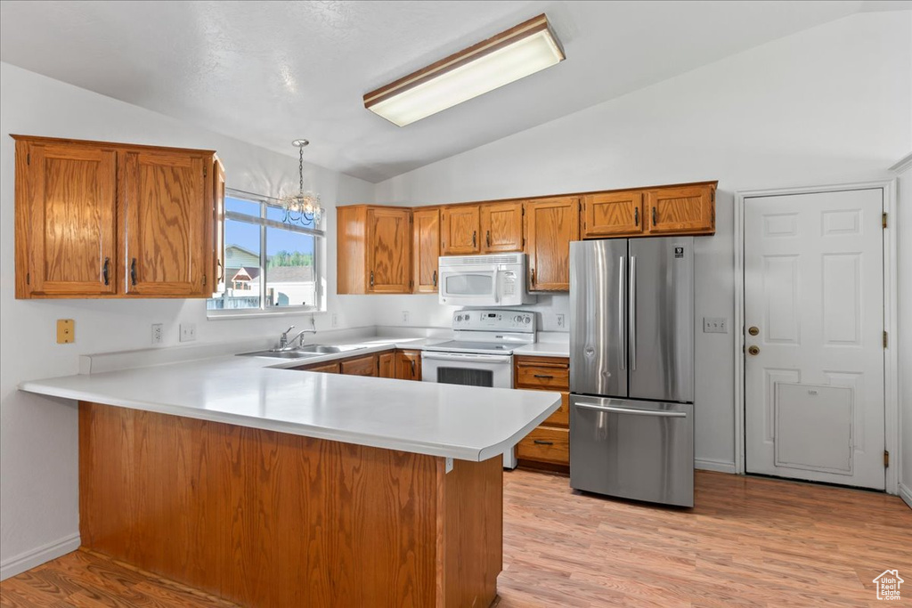 Kitchen with kitchen peninsula, lofted ceiling, pendant lighting, and white appliances