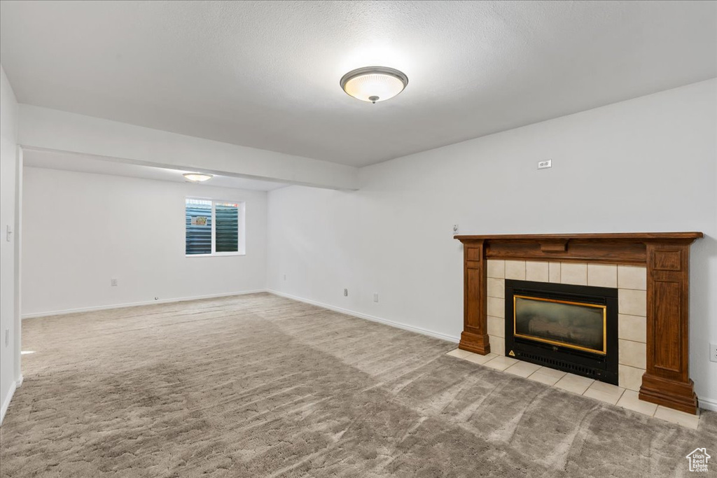 Unfurnished living room with light colored carpet and a tile fireplace