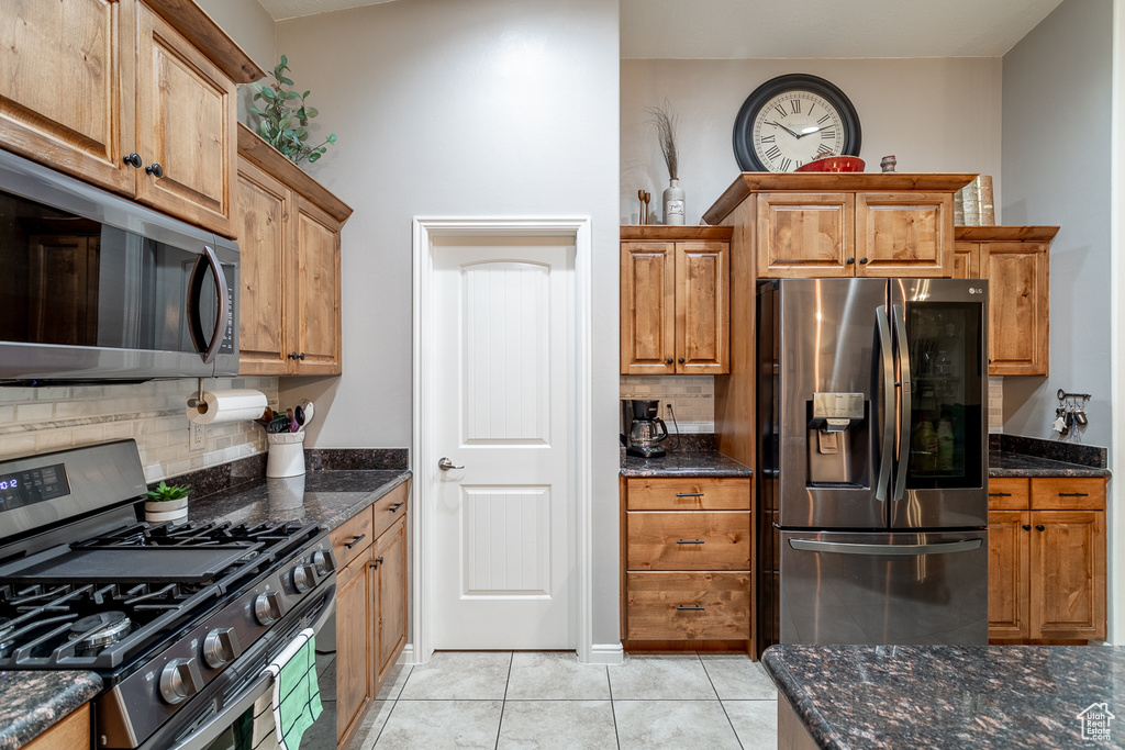 Kitchen featuring light tile patterned flooring, decorative backsplash, appliances with stainless steel finishes, and dark stone counters