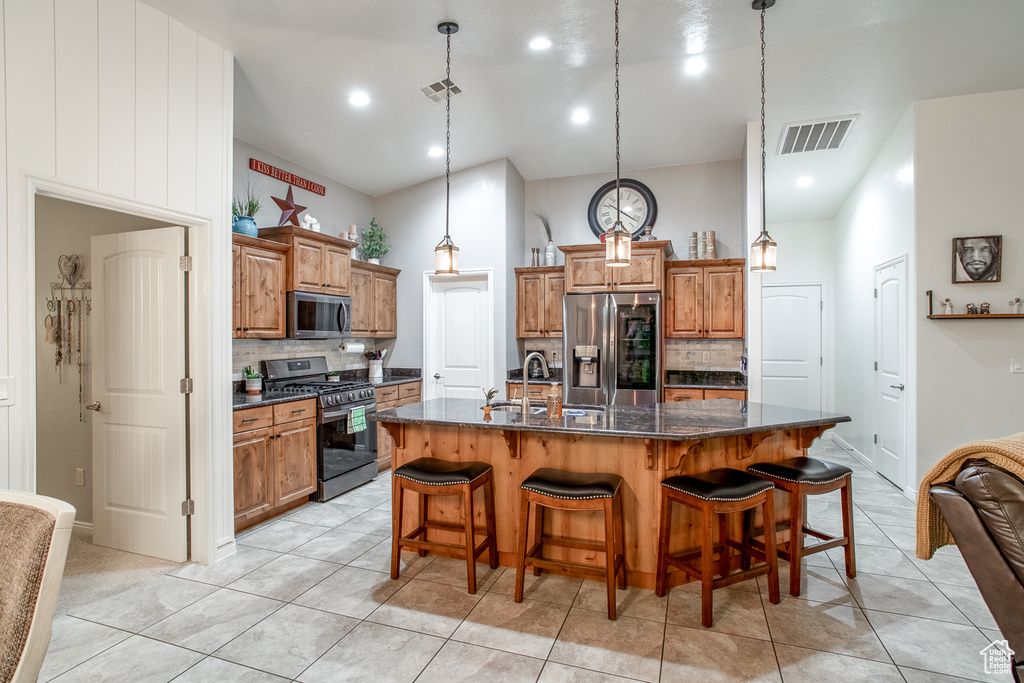 Kitchen featuring stainless steel appliances, decorative light fixtures, backsplash, and a kitchen island with sink