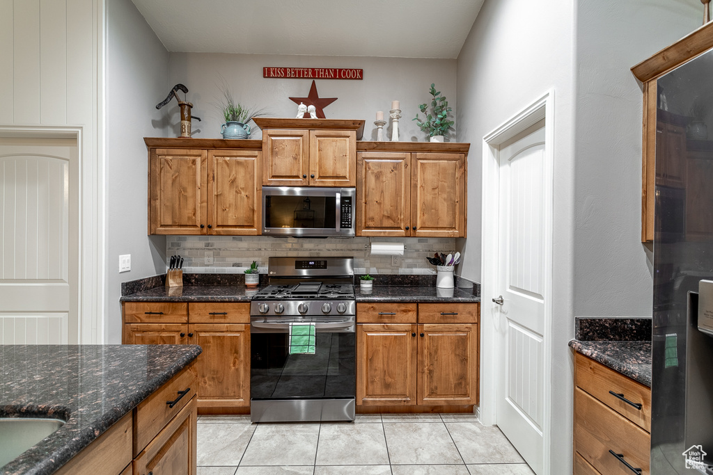 Kitchen with dark stone counters, light tile patterned flooring, backsplash, and stainless steel appliances