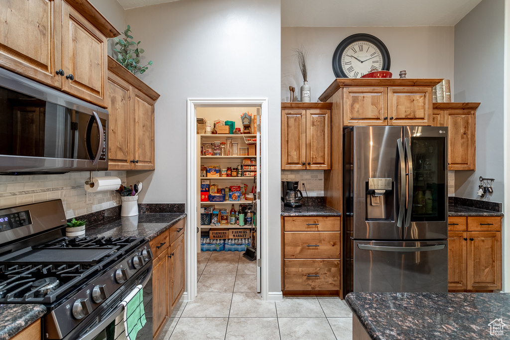 Kitchen featuring light tile patterned flooring, lofted ceiling, dark stone countertops, backsplash, and appliances with stainless steel finishes