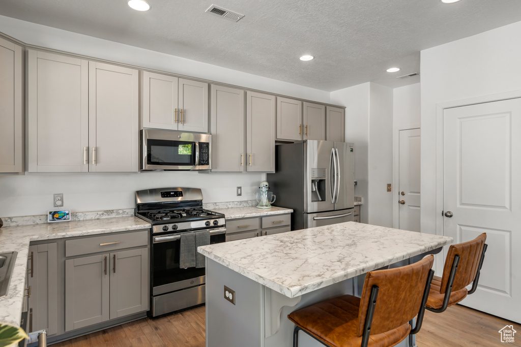 Kitchen with a kitchen island, stainless steel appliances, light wood-type flooring, gray cabinets, and a breakfast bar