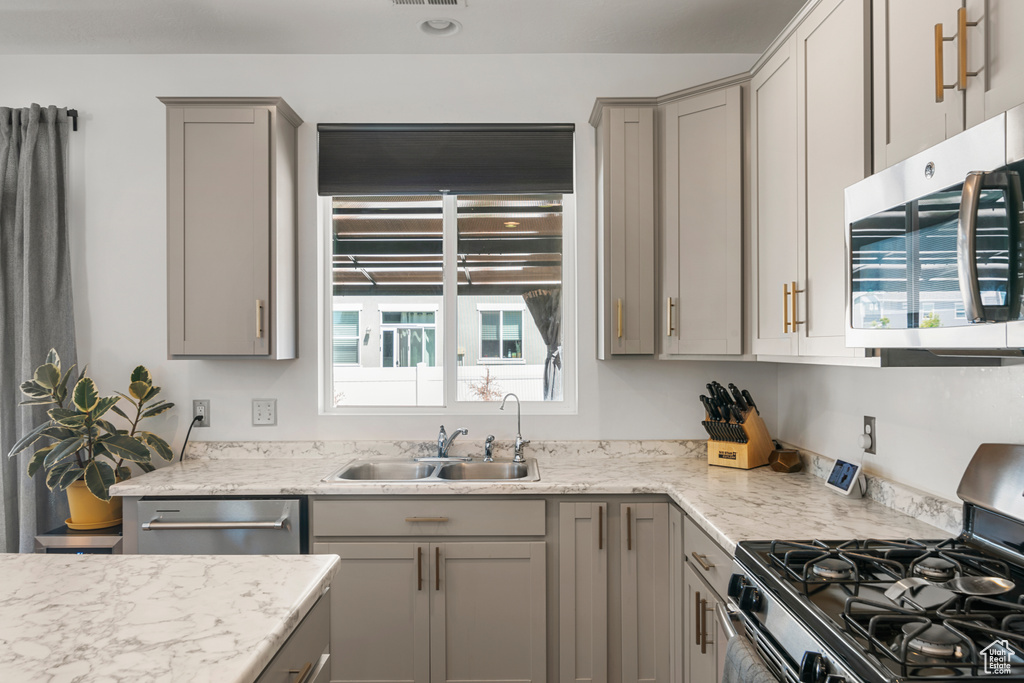 Kitchen with light stone countertops, gray cabinetry, sink, and appliances with stainless steel finishes