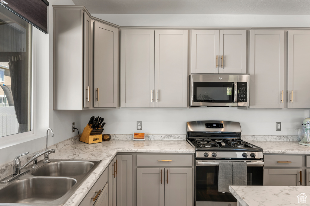 Kitchen with appliances with stainless steel finishes, sink, gray cabinets, and light stone counters