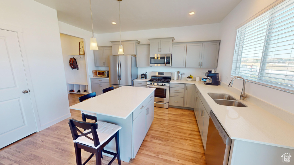 Kitchen featuring stainless steel appliances, hanging light fixtures, sink, a center island, and light hardwood / wood-style floors