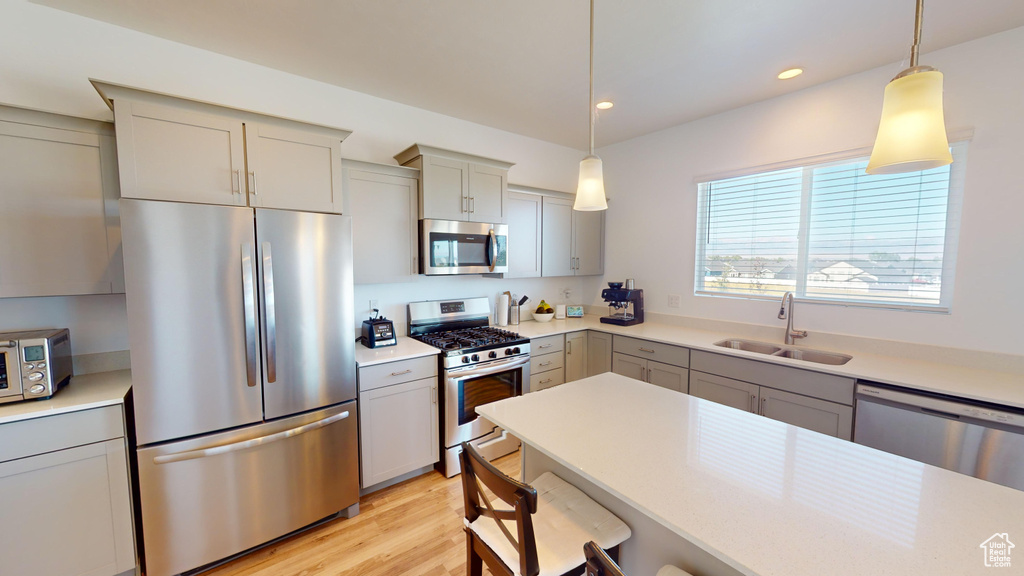 Kitchen with stainless steel appliances, sink, hanging light fixtures, gray cabinets, and light hardwood / wood-style floors