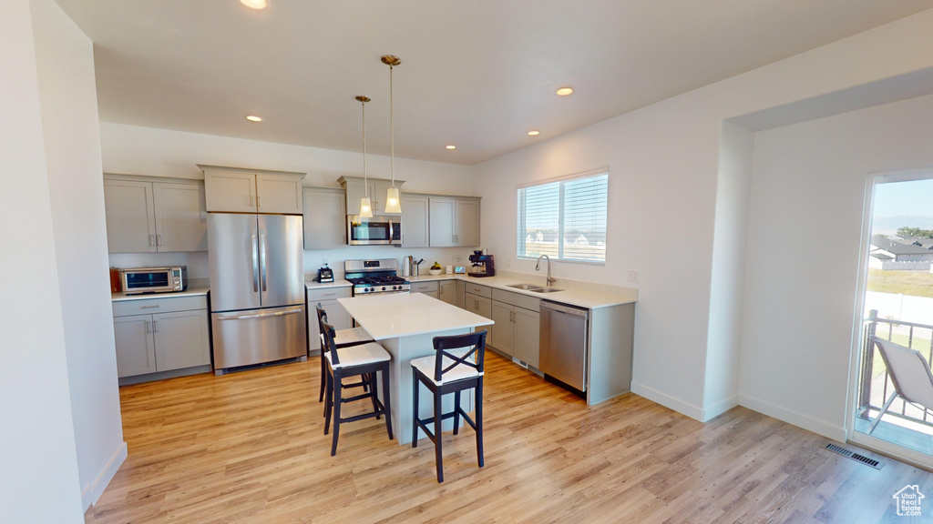 Kitchen with stainless steel appliances, pendant lighting, sink, a center island, and light hardwood / wood-style floors