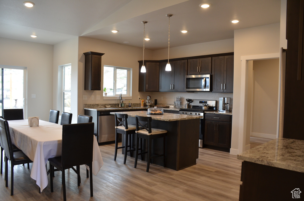 Kitchen featuring light wood-type flooring, a center island, stainless steel appliances, light stone countertops, and decorative light fixtures