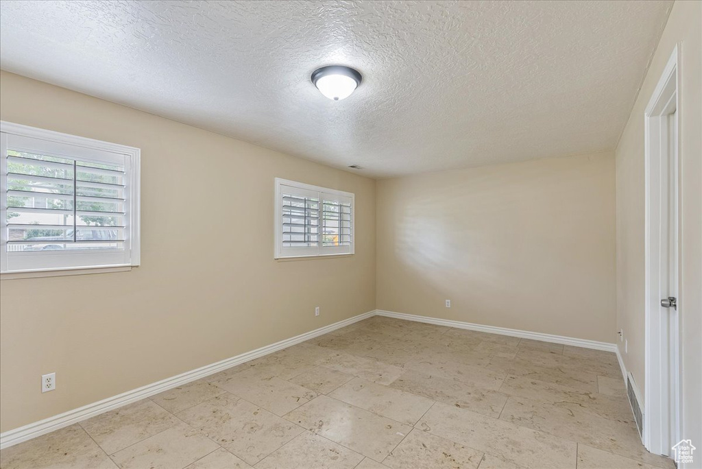 Empty room with light tile patterned flooring, a textured ceiling, and plenty of natural light